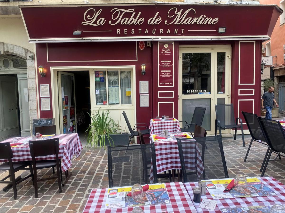 Façade bordeaux du restaurant La Table de Martine et sa terrasse aux nappes à carreaux, place du Marché
